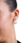 Close-up of a woman's ear wearing a square pearl stud earring with a gold frame, against a transparent background.