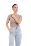 Fashionable woman wearing a fitted taupe top, ripped denim jeans, and bold gold jewelry, showcasing a chic and minimalist style