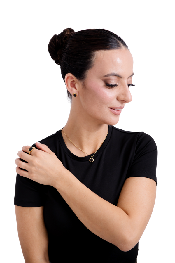 Graceful woman wearing a sleek black outfit, showcasing gold stud earrings, a minimalist necklace, and a stylish gold ring.