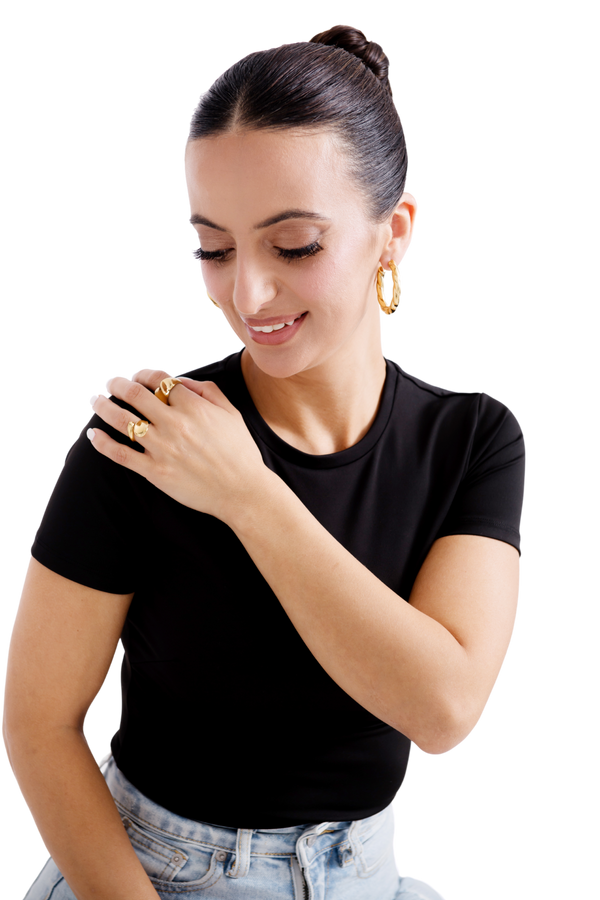 Smiling woman wearing gold hoop earrings and statement rings showcasing elegant jewelry fashion.