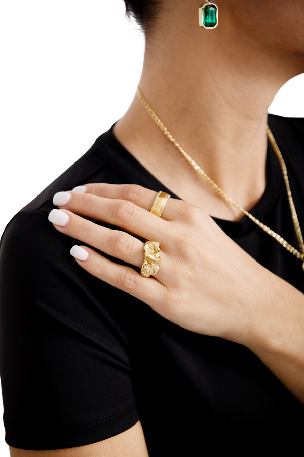 Close up of a woman's hand adorned with elegant gold rings, featuring intricate designs, paired with a gold necklace and an emerald pendant, luxury jewelry fashion.