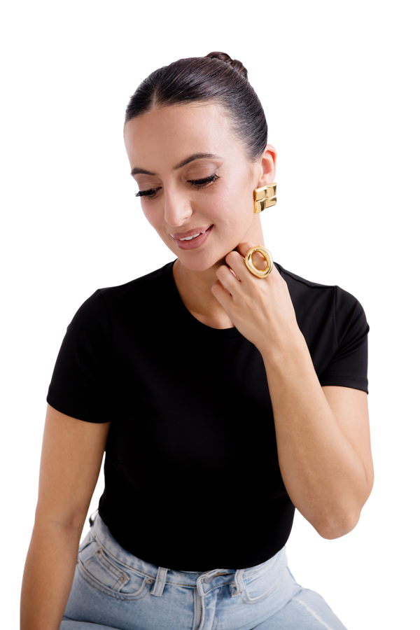 Smiling woman wearing gold hoop earrings and statement rings showcasing elegant jewelry fashion.