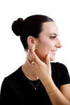 Elegant woman wearing contemporary gold jewelry, including bold sculptural earrings, a matching gold ring, a delicate necklace, and a bracelet, styled with a black top and a sleek updo hairstyle.