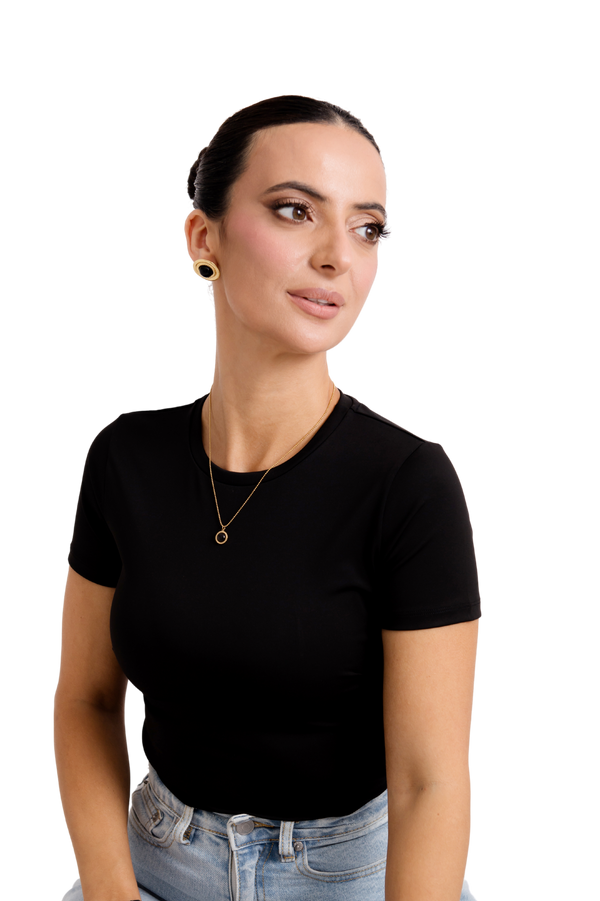 Elegant woman in a black top and denim, wearing gold stud earrings and a delicate gold necklace, exuding modern sophistication.